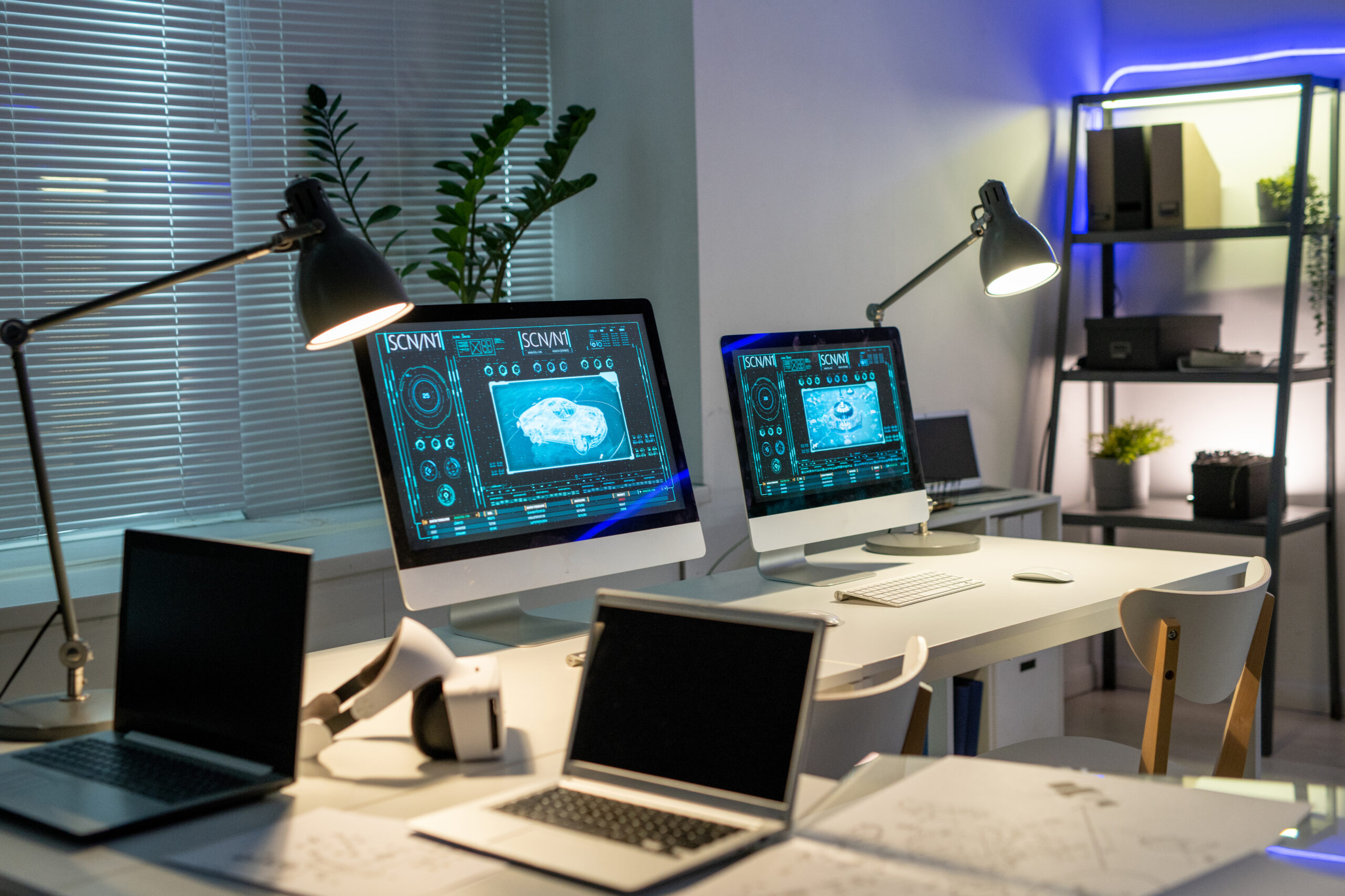 Empty contemporary office of car design company with automobile pictures on computer monitors on tables illuminated with lamps