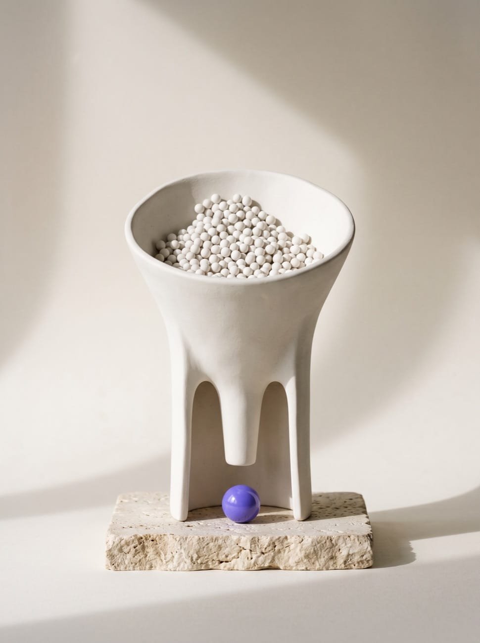 Ceramic funnel full of white spheres releasing a single violet sphere